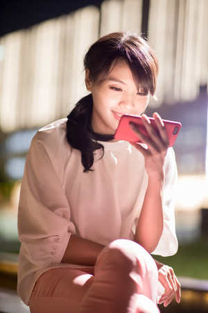 woman use phone and watch video happily with shopping mall at nightの写真素材