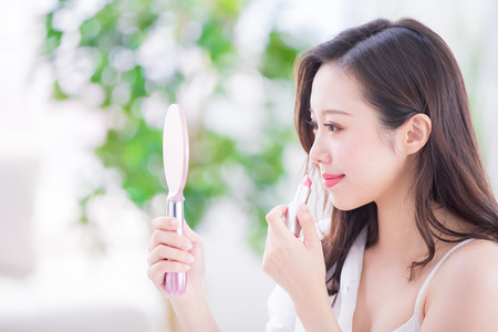 Beauty woman use lipstick and look mirror at homeの写真素材