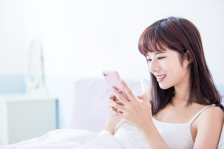 woman use smart phone happily and sit in the bed at homeの写真素材