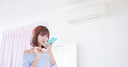 IOT smart home concept - woman talk to smartphone voice assistant and turn on the air conditionerの写真素材