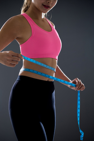 young sports woman measuring waist for weight with tapeの写真素材
