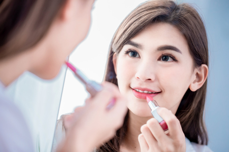 Young beauty woman applying lipstick and looking at mirrorの写真素材