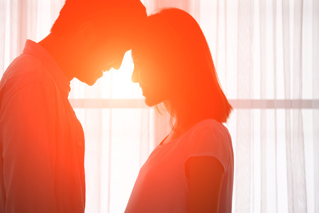 silhouette of sweet couple in front of window at homeの写真素材