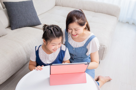 Mom and daughter use tablet happily at homeの写真素材