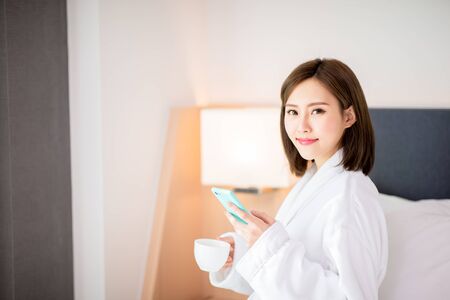 beauty asian woman use smartphone with coffee and enjoy a wonderful morning in the hotelの写真素材