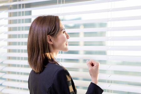 asian businesswoman look window out and cheer for herself in the officeの写真素材