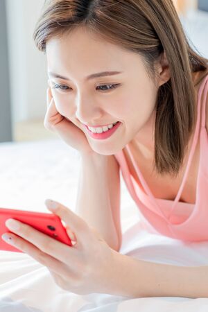 beauty asian woman watch video by smartphone happily on the bed at homeの写真素材