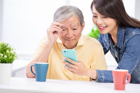 Young daughter teach elder father use mobile at homeの写真素材