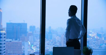 Businessman look through window when work in the nightの写真素材