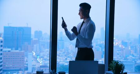 Asian businessman use cellphone exciitedly at night in the officeの写真素材