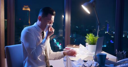 sick asian businesman work overtime and has cough in the officeの写真素材