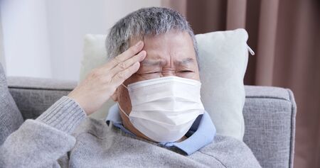 asian eldely sick man feel headache with mask lying on the sofa at homeの写真素材