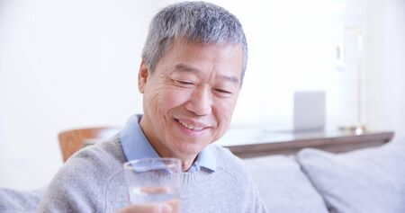 asian old man drink water and feel good at homeの写真素材
