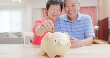 Good Retire plan concept - close up of eldely couple save money to piggy bank smile happily at homeの写真素材