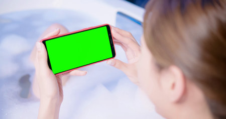 woman watching video by smart phone with green screen while bathing