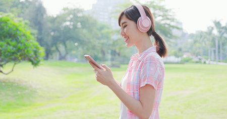 young asian woman listen to music with earphone and her smart phone while walking