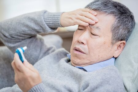 close up of asian eldely man get sick and fever with thermometer lying on the sofa at homeの写真素材