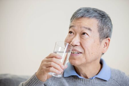 close up of asian old man drink water and feel good at homeの写真素材