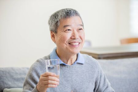 asian old man drink water and feel good at homeの写真素材