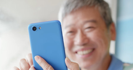close up of asian elder man use smart phone beside windows