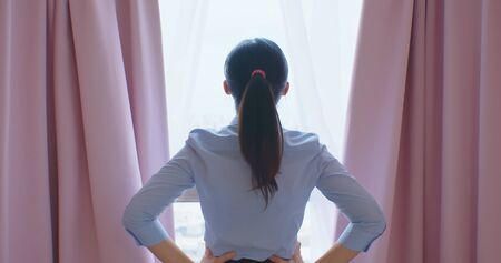 business woman opening curtains and look outside through window in the bedroomの写真素材