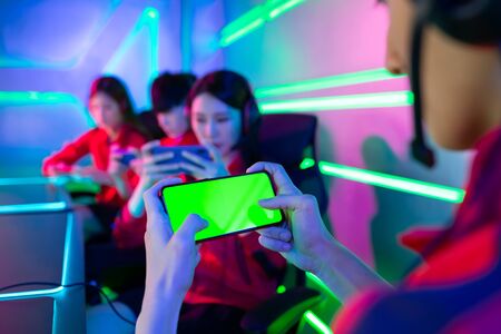 Team of asian teenage cyber sport gamers play mobile game by 5g full display smartphone on eSport tournament with green screenの写真素材