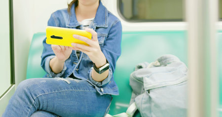 close up of asian young woman play game with 5g smartphone on the mrt or train