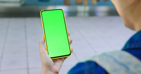 asian young woman use 5g full display smartphone with green screen on the metro station