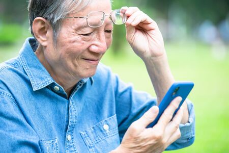 asian elder man has presbyopia and use smart phone in the parkの写真素材