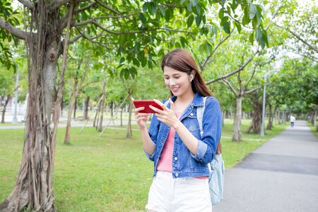 young asian woman watch video and wear wireless earbuds with her smart phone in the parkの写真素材