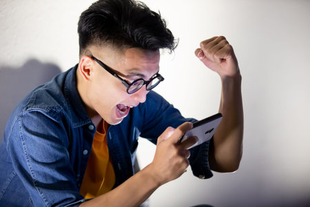 asian young man win mobile games on smart phone with fist gesture outdoor in the evening