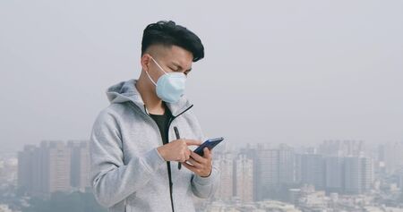 asian man use smartphone and wears protective face mask because of transmissible infectious diseases or air pollution in the cityの写真素材