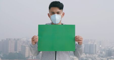 asian man hold green copy space billboard and wears protective face mask against transmissible infectious diseases or air pollution in the cityの写真素材