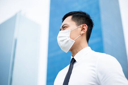 Asian business man with a surgical face mask and he look or think something in front of office buildingの写真素材