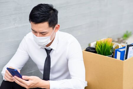 Asian business man wear face mask and search his next job - he is being fired because of economic downturn due to the covid-19 spread all over the worldの写真素材