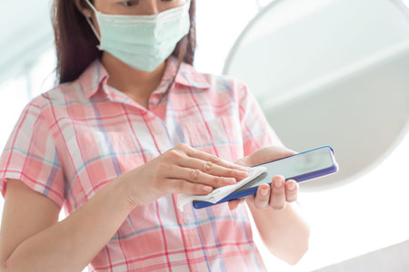 Coronavirus Prevention - woman wiping smartphone on touching surfaces with antibacterial...