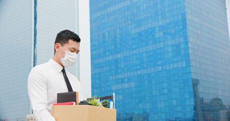 Asian business man wear face mask and he is being fired because of economic downturn due to the covid-19 spread all over the worldの写真素材