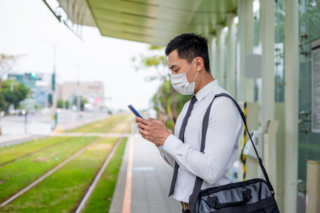 Asian business man use a smartphone with surgical mask face protection while waiting the metro or...