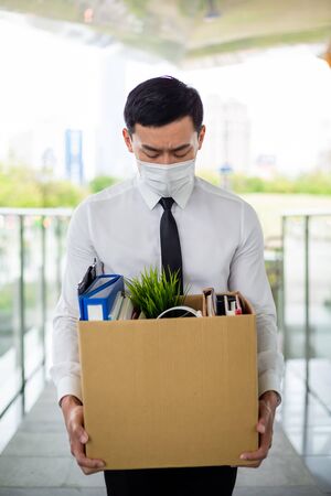 Asian business man wear face mask and he is being fired because of economic downturn due to covid-19 spread all over the worldの写真素材