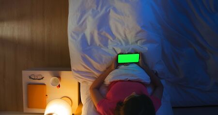 Overhead view of asian woman watch video by smartphone with green screen on the bed in the roomの写真素材