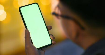 back view of asian young man watch smart phone with green screenの写真素材