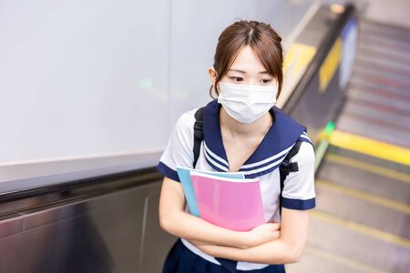 Asian girl high school student take escalator in the mrt station and wear face maskの写真素材