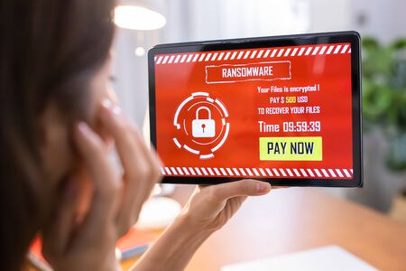 back view of asian worried young woman looking at tablet pc with ransomware attack words on the screen at homeの写真素材