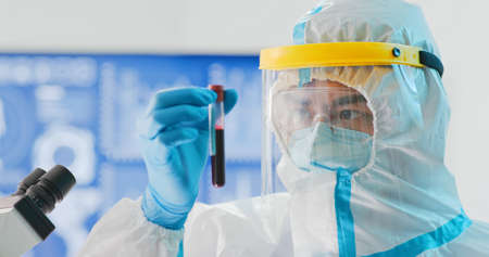 asian male scientist researcher holding a positive blood test result for the Coronavirus with isolation gown or protective suits and surgical face maskの写真素材