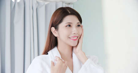 beauty asian girl touch her good skin on face and look mirror in the bathroomの写真素材