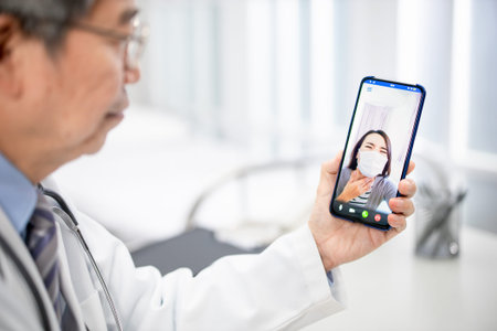 Telemedicine concept-asian senior male doctor explain to the patient about the disease by video chat on cell phone in hospitalの写真素材