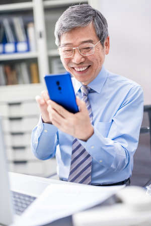 asian elder businessman use smartphone happily in the officeの写真素材