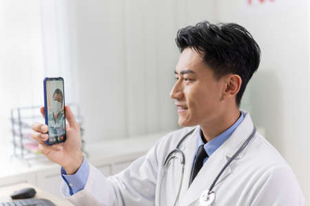Telemedicine concept-asian young doctor is listening to elder male patient on smart phoneの写真素材
