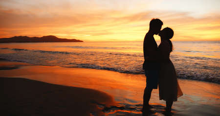 silhouette of asian couple holding each other hands and standing on the beach during sunsetの写真素材