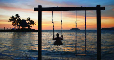 asian girl play the swing at the seaside in eveningの写真素材